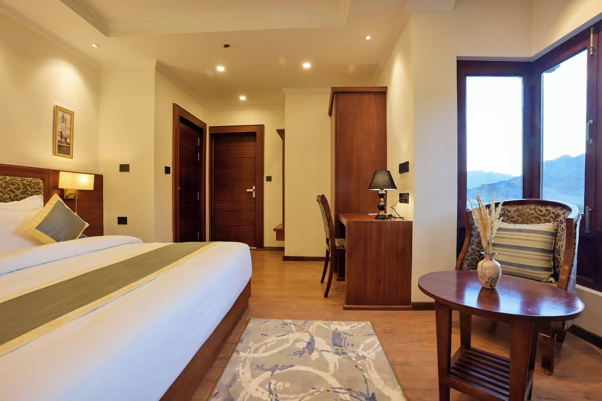 A hotel room with a bed, a desk, a chair, and a view of mountains.