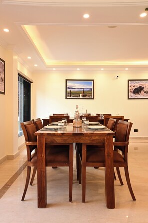 A dining area with a wooden table and chairs, framed pictures on the walls, and a window on the left.