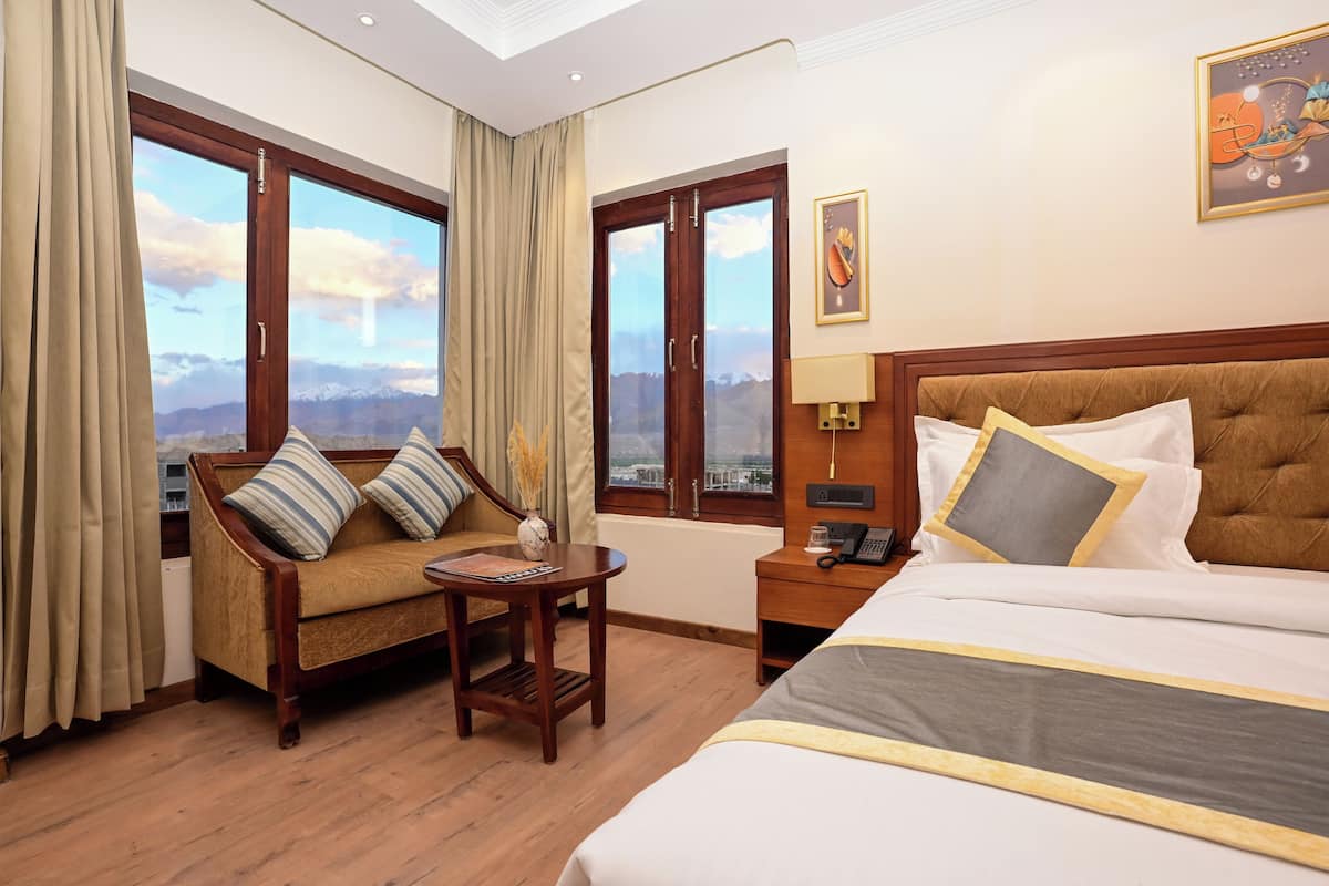 A hotel room with a bed, a sofa, a small table, a nightstand, and large windows with a mountain view.