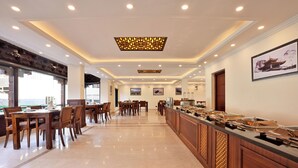 Un comedor de hotel con varias mesas y sillas, un mostrador de buffet e iluminación empotrada en el techo.