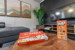Un salon avec un canapé gris, une table basse, une boîte de jeu de Scrabble, une boîte de jeu de Jenga et un téléviseur.