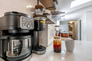 Una cocina con cafetera, microondas y un tarro de té helado sobre la encimera.