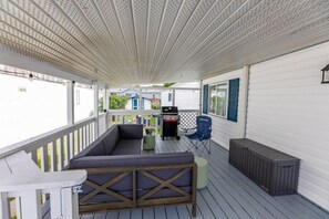 Une véranda couverte avec un coin salon agrémenté de coussins, un barbecue et une chaise.