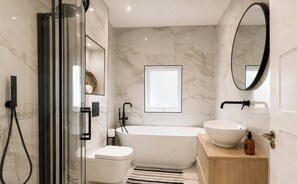 A modern bathroom with a glass shower enclosure, a freestanding bathtub, a white sink, and a large mirror. - Exclusive 2 Bedroom House in Catford! (London)