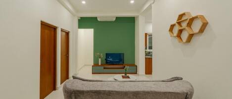 A hallway with a grey sofa, a TV on a wooden stand, and a green wall.