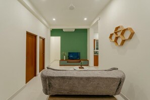 A hallway with a grey sofa, a TV on a wooden stand, and a green wall. - Mulberry Living  (Negombo)