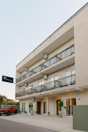 Un hotel de diversos pisos amb balcons, un cotxe a davant i un cartell.