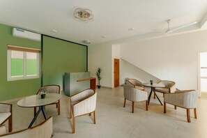 A modern hotel room with a green accent wall, a dining area with round tables and chairs, a staircase, and a ceiling fan. - Mulberry Living  (Negombo)