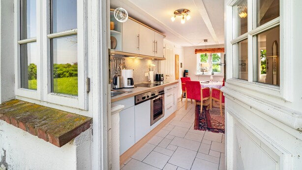 A compact kitchen with white cabinets, a built-in oven, and a dining area with a red tablecloth. - Apartment "Kiel" with Shared Terrace, Garden, and Wi-Fi (Pellworm)