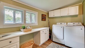 Ein Waschraum mit zwei weißen Waschmaschinen und Trocknern, einem Fenster mit Jalousien, einem Korbwäscheschrank und einem gemusterten Teppich.