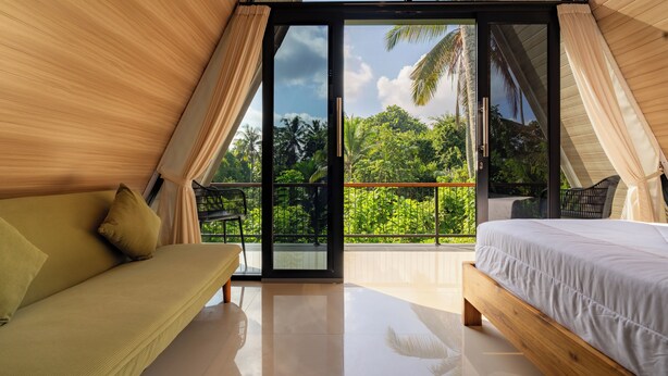 Un dormitorio moderno con sofá, cama y balcón con vistas a la vegetación.