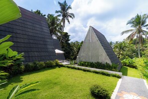 Un edificio moderno con techo oscuro, rodeado de exuberante vegetación y palmeras.