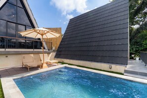 Un edificio moderno con piscina, sillas de descanso y un gran paraguas.