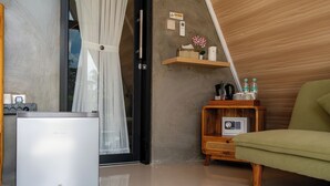 Una habitación con un refrigerador compacto, una mesita de noche de madera con una radio y una silla verde.