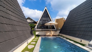 Una piscina con diseño de casa moderna, cielo despejado y valla de madera.