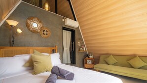 Una habitación con cama, sofá verde, aire acondicionado de pared, lámpara y espejo decorativo.