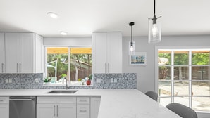A modern kitchen with white cabinets, a marble countertop, and a large window. - 5BR Group Retreat w/ Pool in Austin, 4 Mi to Dtwn (Austin)