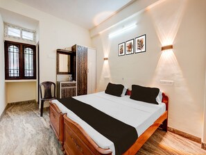 Um quarto com cama, penteadeira, cadeira, espelho e luminárias fixadas na parede.