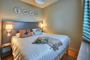 Una cama bien hecha con una revista, almohadas y una lámpara en una mesita de noche.