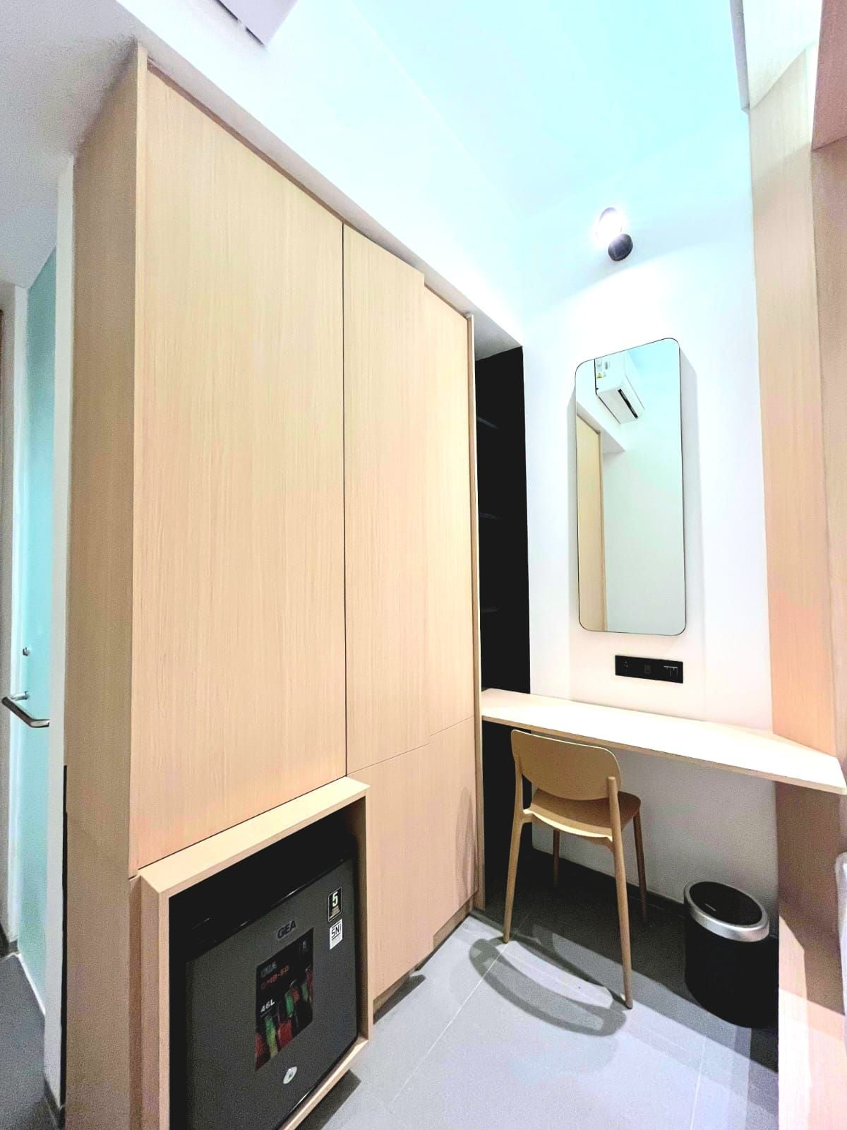 Une pièce de taille modeste, avec une armoire en bois, un bureau avec une chaise, un petit radiateur et un miroir au mur.