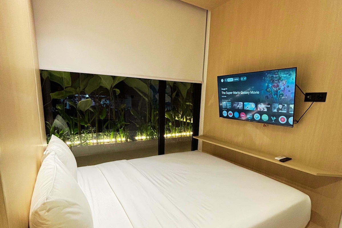 Ein modernes Hotelzimmer mit einem Bett, einem an der Wand befestigten Fernseher, der einen Film zeigt, und einem Fenster mit Blick auf Grünflächen.