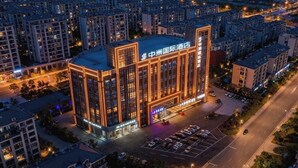 Un hotel moderno con un cartello ben visibile, circondato da altri edifici e un parcheggio.