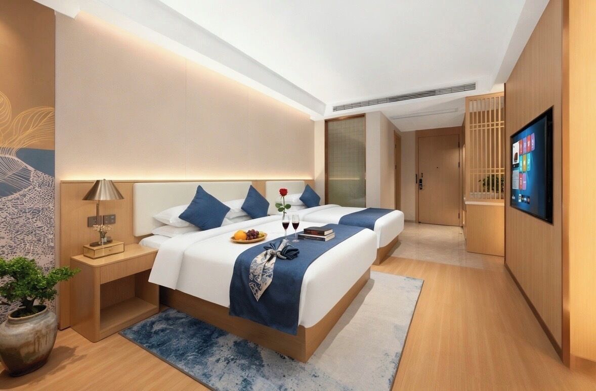Ein modernes Hotelzimmer mit zwei Betten, einem Fernseher, einem Nachttisch mit Lampe und einer kleinen Pflanze.