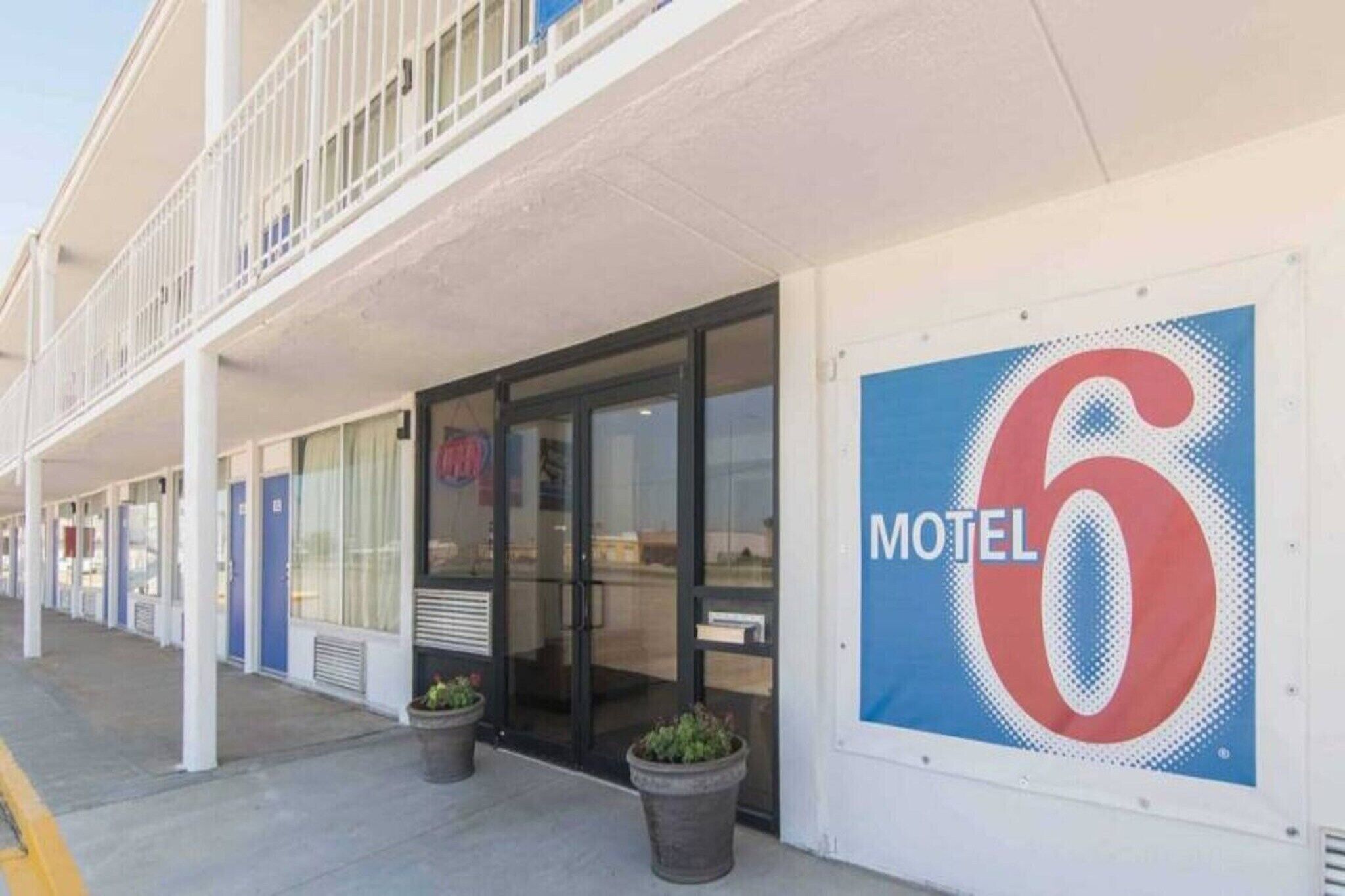 Un motel con un letrero grande con el número 6, un corredor cubierto y plantas en macetas en la entrada.