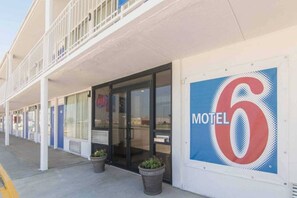 Un motel con un letrero grande con el número 6, un corredor cubierto y plantas en macetas en la entrada.