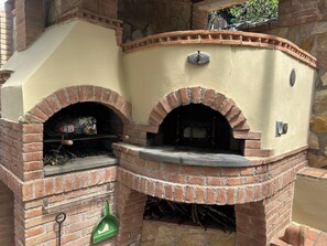 A brick-built outdoor oven with a chimney, a green shovel, and a metal door. - The rustic-little country house (Liguria)