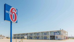 Um motel com um letreiro grande com o número '6', um edifício de dois andares com teto plano e um letreiro 'ABERTO'.