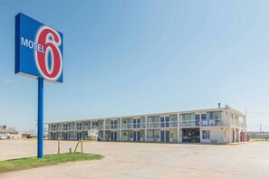Un motel con un letrero grande con el número '6', un edificio de dos pisos con techo plano y un letrero que dice 'ABIERTO'.