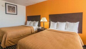 Quarto de hotel com duas camas, mesa de cabeceira com abajur e quadro pendurado na parede.