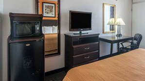 A hotel room with a bed, a desk with a lamp, a television, and a microwave.