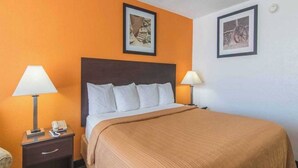 Een hotelkamer met een bed, twee bedlampjes, een nachtkastje met een telefoon en twee ingelijste foto's aan de muur.