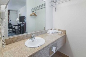 A hotel bathroom with a granite countertop, a white sink, a mirror, a towel rack, and a television in the background. - 1 King Bed|Smoking,Micfridge (Liberal KS)
