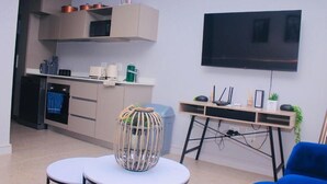 A modern kitchen with a microwave, oven, and cabinets, a dining area with a table and chairs, and a TV mounted on the wall. - Zimbali lakes boulevard edge 103 (Ballito)