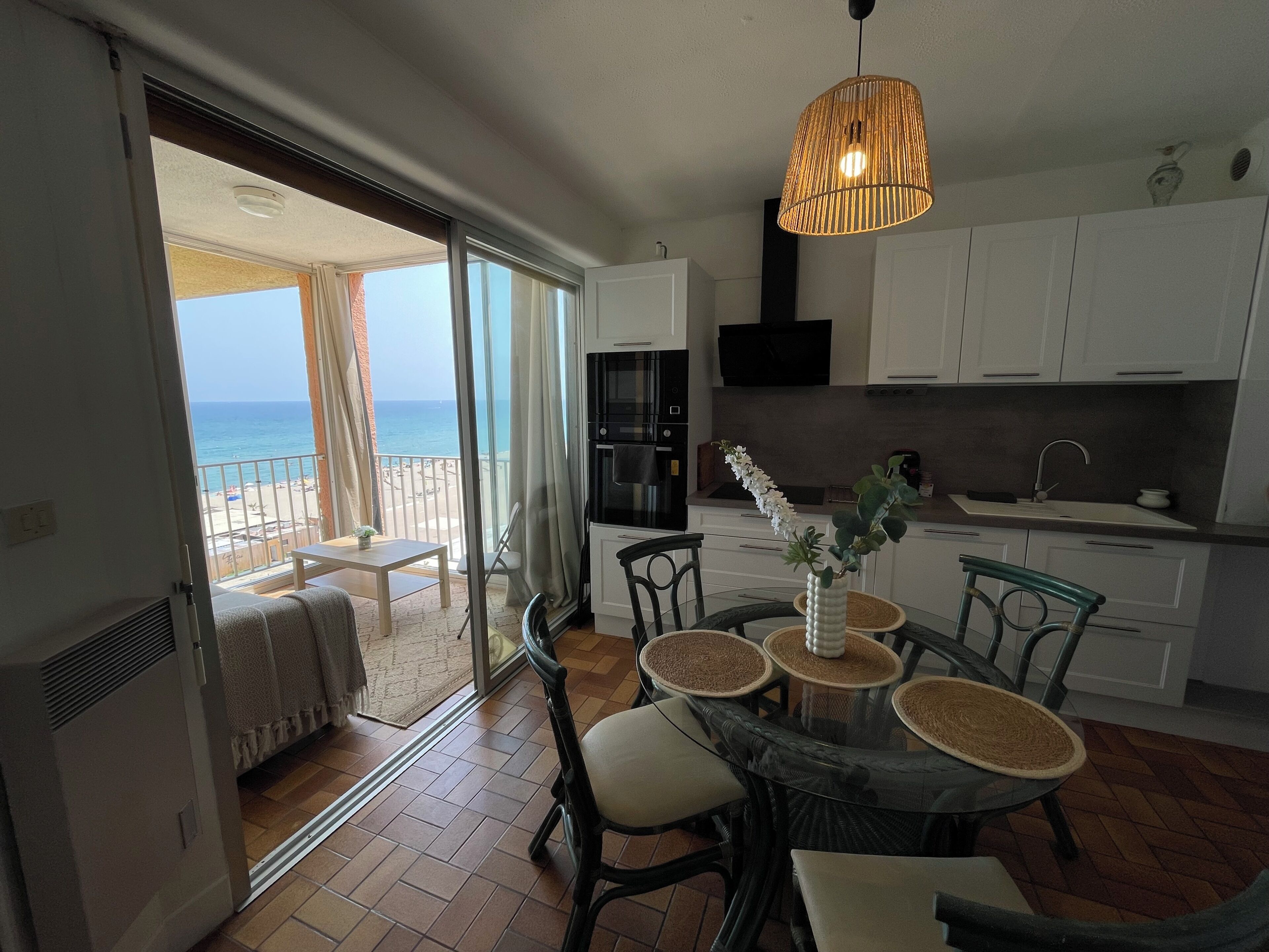 A modern kitchen with white cabinets, a black oven, and a dining area with a glass table and chairs.