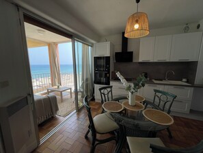 A modern kitchen with white cabinets, a black oven, and a dining area with a glass table and chairs. - STUNNING APARTMENT WITH OCEAN VIEW (Le Barcarès)