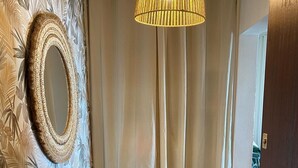 Et værelse med tapet, et rundt spejl, en vævet måtte og en loftlampe.