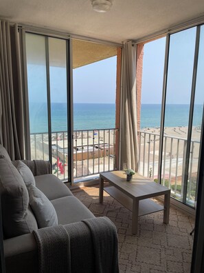 Ein Balkon mit Blick auf den Strand, einer Couch und einem kleinen Tisch.