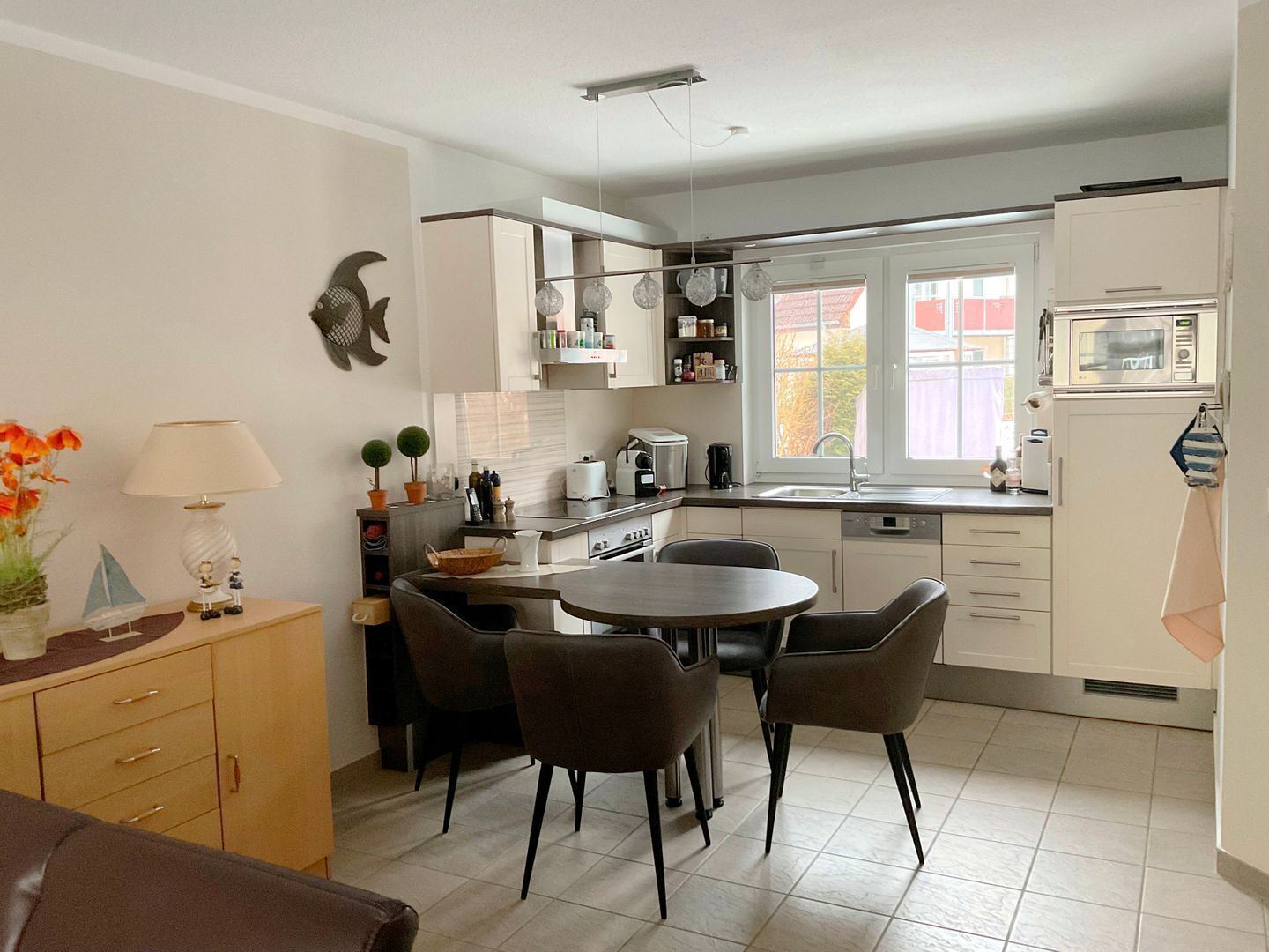 Une cuisine moderne avec un coin repas, des meubles blancs, un four à micro-ondes et une fenêtre laissant entrer la lumière naturelle.