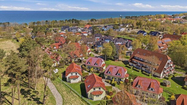 Luchtbeeld van een woonwijk met huizen, een heldere lucht en een waterpartij op de achtergrond.