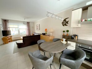 Ein modernes Wohnzimmer mit Sofa, Esstisch und Stühlen, einem Küchenbereich mit Schränken und Geräten sowie einem Fernseher.