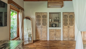 A room with wooden flooring, a mirror, a wardrobe, and a shelf with decorative items.
