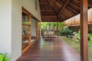 A covered wooden deck with a bench, glass doors, and a thatched roof. - Villa Chempaka Chill by Alfred in Bali (Canggu)