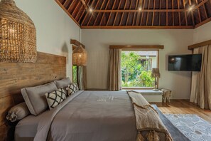 A bedroom with a large bed, wooden ceiling, a TV, and a window with a view of greenery. - Villa Chempaka Chill by Alfred in Bali (Canggu)