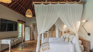A room with a four-poster bed, wooden flooring, a bench, and a hanging light fixture.