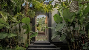 A pathway leading to a structure with an archway, surrounded by lush tropical vegetation.