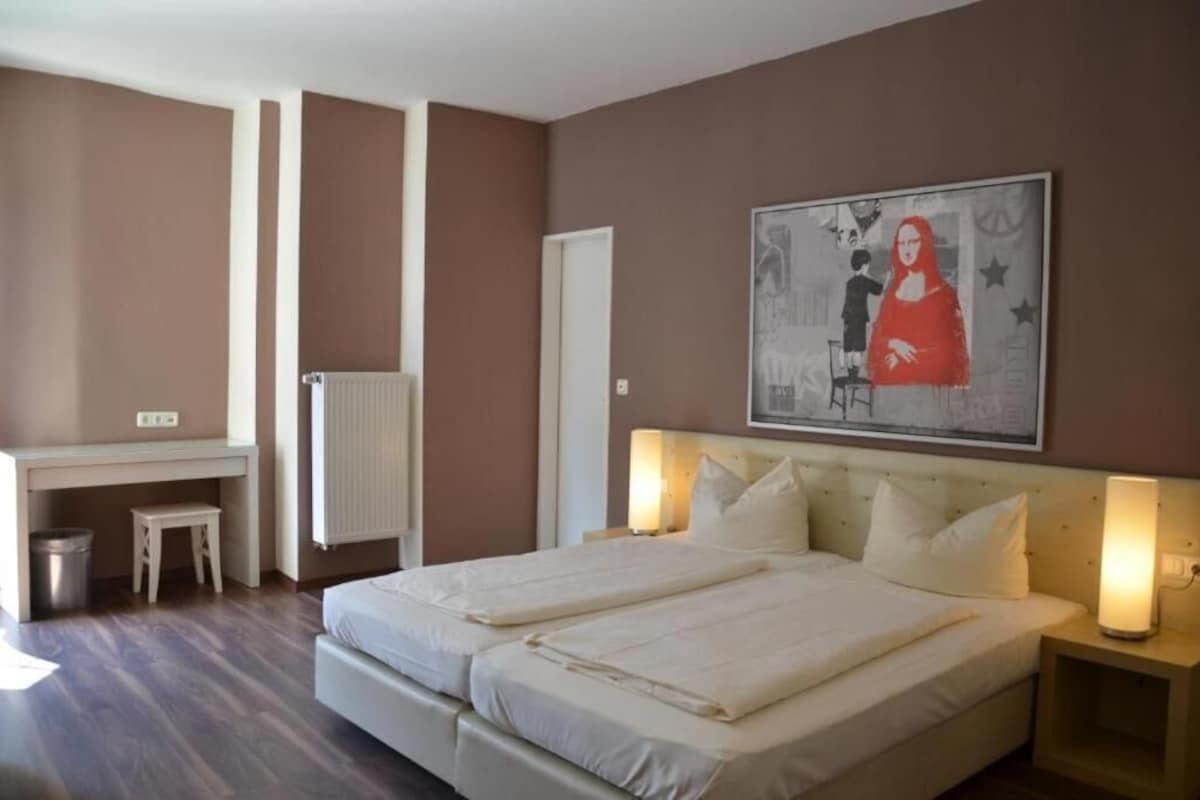 A bedroom with a bed, bedside tables, a desk, and a radiator.